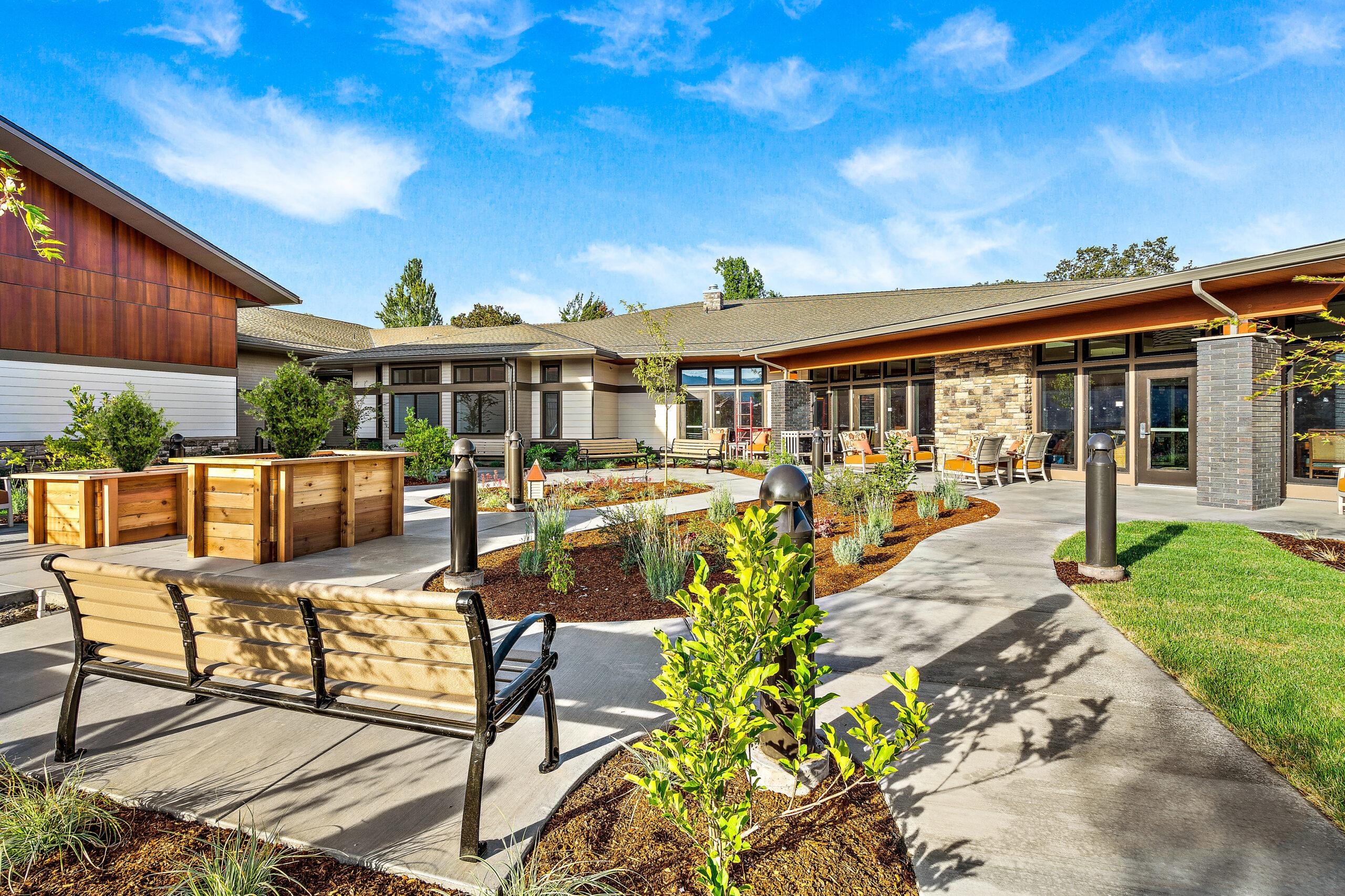 An outdoor shot of a Rogue Valley Manor residence with sidewalks, benches and gardens.