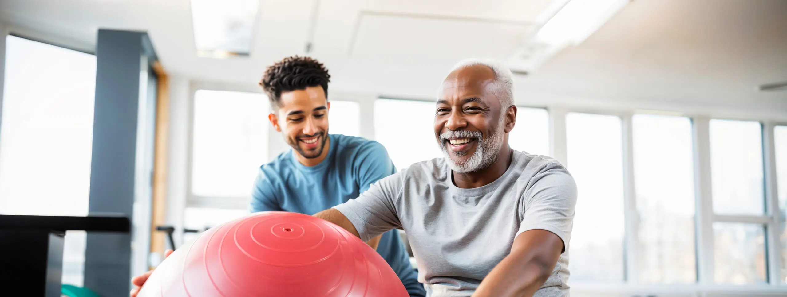 A physical therapist does a physiotherapy exercise with an older patient using an exercise ball.